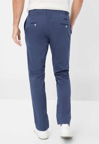Pantaloni casual blu navy realizzati in tessuto leggero. Presentano tasche posteriori con chiusura a bottoni. Indossati con sneakers bianche.