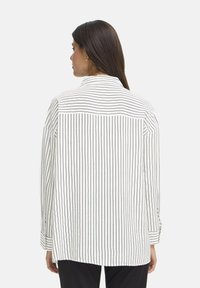 White striped shirt with long sleeves, a back yoke, and buttoned cuffs. Features vertical navy stripes and a relaxed fit.
