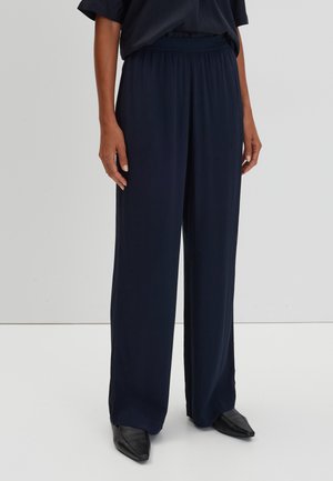 Marinefarbene weite Hosen aus weichem Stoff mit elastischem Bund, die eine glatte Textur und ein langes Design aufweisen, kombiniert mit schwarzen Schuhen.
