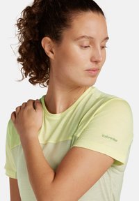 Camiseta deportiva de color amarillo claro con mangas cortas, que presenta un diseño bicolor, una textura suave y un logo verde de "icebreaker" en la manga.