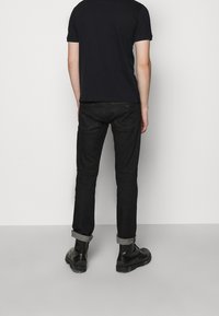 Černé džíny slim fit s ohrnutými nohavicemi a zadními kapsami. Kombinované s černým tričkem s krátkým rukávem a černými botami.