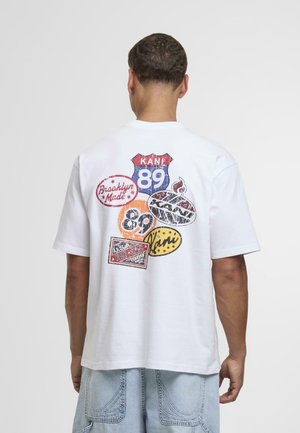 White short-sleeve t-shirt featuring colorful printed patches and text on the back, including shapes like circles and a highway sign.