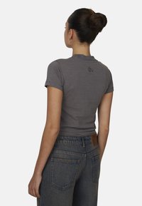 Grijze fitted t-shirt met korte mouwen en een ronde hals, met een klein logo op de achterkant. Draag het met high-waisted blauwe denim jeans.