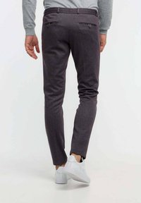 Strakke donkergrijze broek van gestructureerde stof, met twee achterzakken met knopen en een slank pasvorm. Gedragen met witte sneakers.