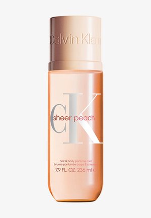 Brume parfumée pour les cheveux et le corps CK Sheer Peach dans un flacon transparent pêche, avec un capuchon métallique et une inscription argentée et rouge bien visible.