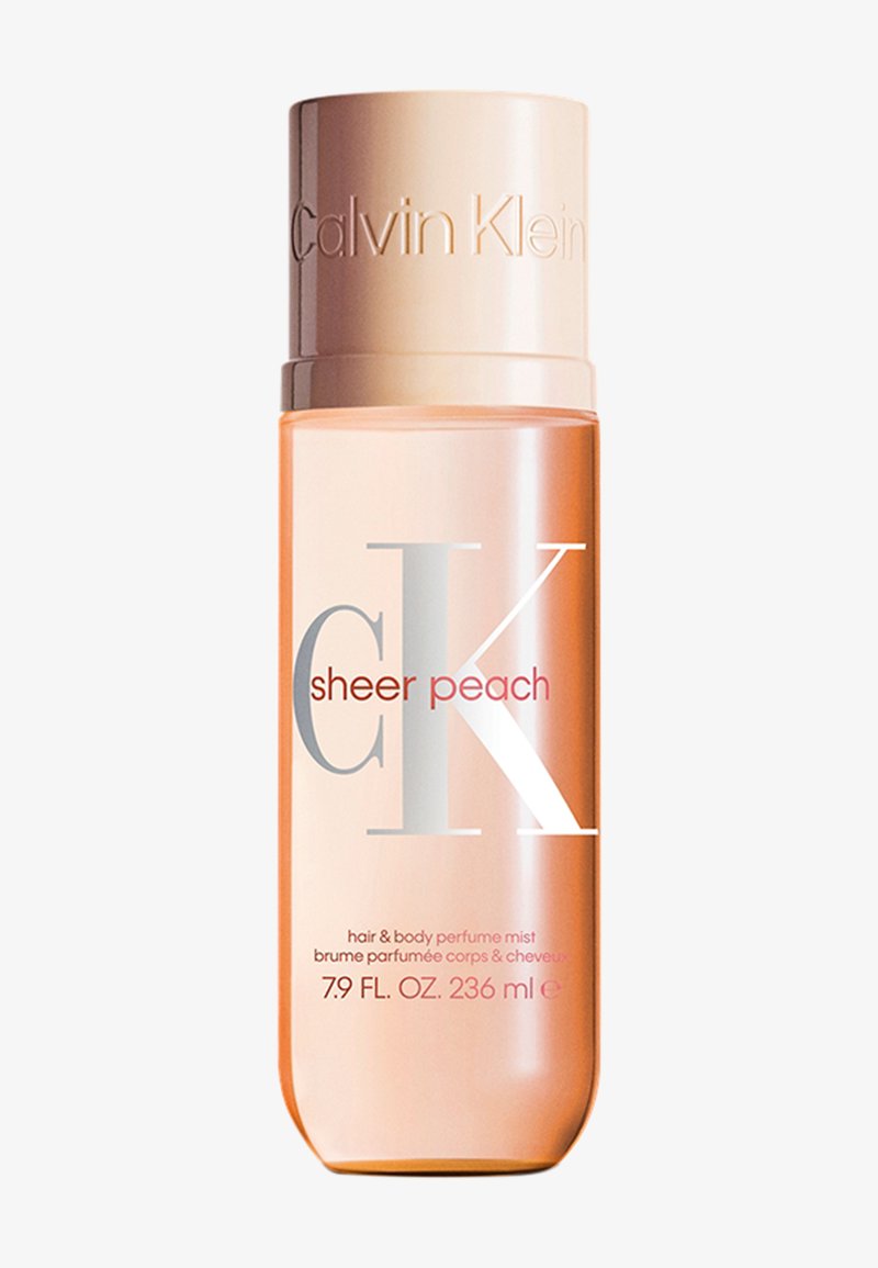 Brume parfumée pour les cheveux et le corps CK Sheer Peach dans un flacon transparent pêche, avec un capuchon métallique et une inscription argentée et rouge bien visible.