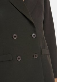 Donkergroene dubbelzijdige blazer van textiel; voorzien van revers, twee voorzakken en grote zwarte knopen.