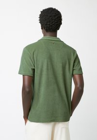 Groene polo met korte mouwen, gemaakt van zachte, getextureerde stof, met een kraag en een knoopdetail aan de achterkant.