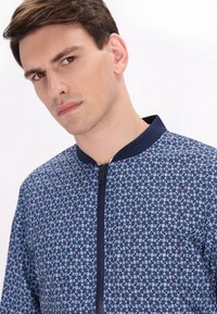 Reißverschluss-Bomberjacke mit einem blauen Blumendruck und roten sowie grünen Akzenten. Hergestellt aus einem Stoff mit glatter Textur und geripptem Kragen.