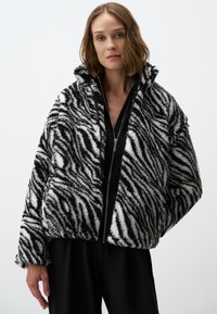 Zwart-wit gestreepte zebra-fur jas met een rits aan de voorkant en hoge kraag; zachte, pluizige textuur; oversized ontwerp.