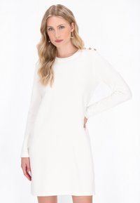 Abito bianco a maniche lunghe con scollatura rotonda e quattro bottoni decorativi sulla spalla. Tessuto morbido con una vestibilità comoda.