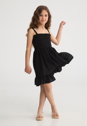 Vestito nero senza maniche con corpino arricciato e orlo a volant, realizzato in tessuto testurizzato. Il design presenta spalline regolabili e una silhouette fluida.