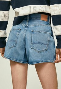 Denim shorts i ljusblått med hög midja och rå nederkant. Bakfickorna har subtila sömnadsdetaljer. Tyget har en mjuk textur.