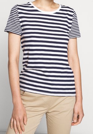 T-shirt en coton à rayures bleu marine et blanches, col rond et manches courtes ; texture lisse et coupe décontractée, porté avec un pantalon beige.