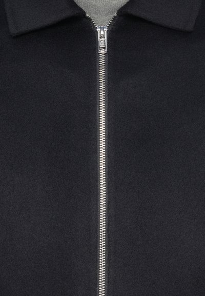 Fekete gyapjúkeverék dzseki cipzáras záródással, gallérral és puha tapintással. Fém cipzáras díszítésekkel az elején.