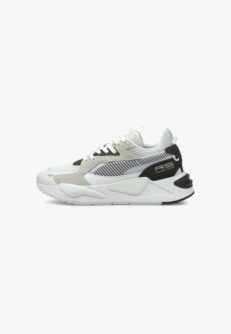 Zapatillas con parte superior de malla blanca y ante, adornadas con acentos en negro y gris. Suela blanca gruesa con detalles texturizados y marca visible en los laterales.