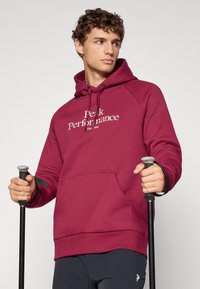 Mørkerød hættetrøje med "Peak Performance" logo, kengurulomme, snoretræk og ribbede manchetter, kombineret med vandrestave.