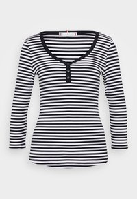 Musta-valkoinen raidallinen pitkähihaisen paita, jossa on V-pääntie ja kolme napin läppää. Ribboneulosta ja pyöristetty helmaliuska.