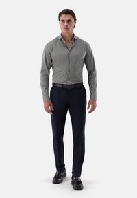 Camicia a maniche lunghe a righe verde scuro e bianca, vestibilità attillata, abbinata a pantaloni eleganti blu navy e scarpe di pelle nere.