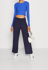 Blå randig långärmad crop top som bärs tillsammans med marinblå vida byxor. Vita sneakers med svarta ränder; håller en vit handväska.