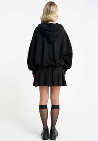 Czarna, oversize'owa bluza z kapturem, zestawiona z czarną plisowaną mini spódnicą, skarpetami do kolan i masywnymi czarnymi butami.