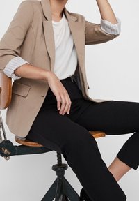 Beżowa marynarka o strukturalnym fasonie, z klapami w kształcie litery V i podwiniętymi mankietami. Połączona z białą koszulą i czarnymi spodniami.