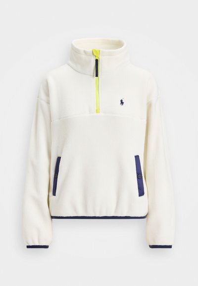 Fehér gyapjú pulóver fél cipzárral elöl, tengerészkék részletekkel a zsebeknél és az alján, valamint egy élénk sárga cipzárhúzóval. Kis logó található a mellkason.