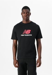 Fekete pamut póló, melyen feltűnően piros és fehér "New Balance" logó látható. Rövid ujjú és klasszikus kerek nyakú dizájn.