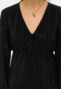 Sort plisssert bluse med dyp V-utringning, justerbart bånd i midjen og lange ermer. Har en silkeaktig tekstur og subtil glans.