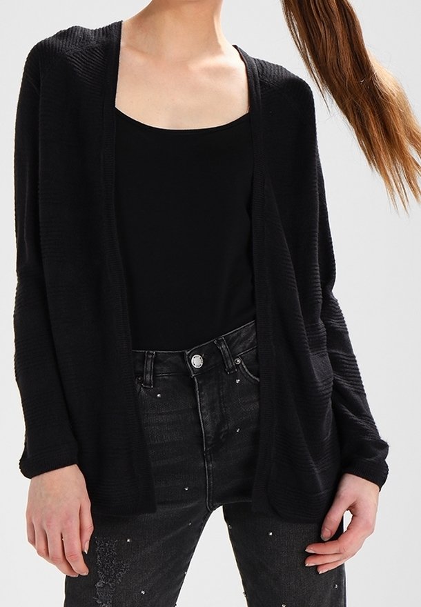 Czarny sweter z dzianiny z otwartym przodem, teksturowanym wzorem i długimi rękawami, noszony na czarnej bluzce, w połączeniu z ciemnymi dżinsami z ozdobnymi detalami.