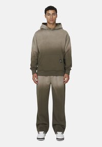 Hoodie en bijpassende broek in een ombre olijfgroen. Bevat een voorzak, textuur stof en een relaxte pasvorm. Witte sneakers maken de look compleet.