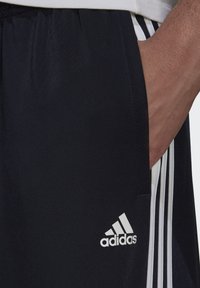 Marineblaue Sportshorts aus synthetischem Material, mit weißen seitlichen Streifen und einem gestickten weißen Adidas-Logo am unteren Saum.