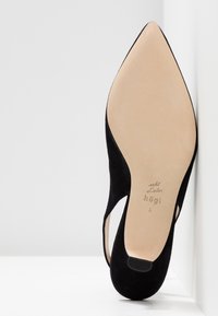 Chaussure slingback noire en daim à bout pointu avec semelle en cuir beige et nom de la marque "högl" embossé sur la semelle.