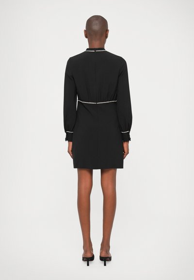 Vestido negro con mangas largas, cintura ajustada y un borde decorativo plateado a lo largo del escote y las mangas, con un corte a la altura de la rodilla.