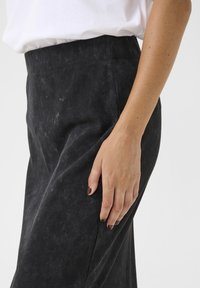 Black corduroy high-waisted pants, featuring soft texture and subtle ribbing, with a hand resting on the side for scale.