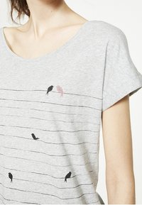Camiseta gris de manga corta con cuello redondo y rayas horizontales negras que presenta cuatro ilustraciones de pájaros en varias posturas y colores.