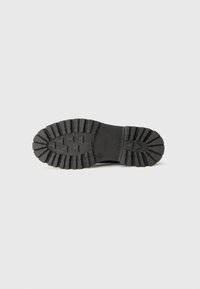 Suola di scarpa nera in gomma con profondi intagli e motivi angolati per la presa. Design piatto con superficie liscia e bordi arrotondati.