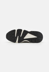 Černá gumová podešev s texturovanými vzory, kontrastní bílá mezipodešev a detail loga Nike Air.