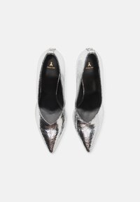 Zapatos de tacón alto plateados con un exterior de cuero texturizado y agrietado y punteras puntiagudas. Interior negro con detalles del logotipo en dorado.