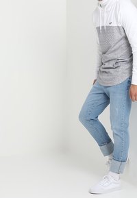 Ljusgrå och vit långärmad hoodie med snörning, tillsammans med ljusblå uppvikt jeans och vita sneakers. Avslappnad, ledig passform.