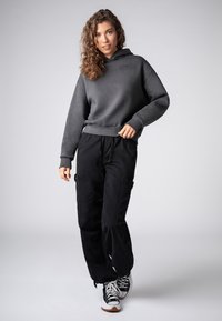 Grijze hoodie met een voorkeurszak, gecombineerd met zwarte cargobroeken met zijzakken en zwart-witte sneakers.