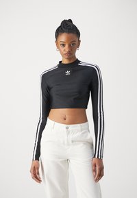 Top preto cropped de mangas longas com colarinho alto, apresentando riscas brancas nas mangas e um logo da adidas no peito. Tecido suave.