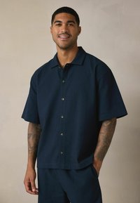 Tengerészkék, rövid ujjú gombos ing, texturált anyagból, két elülső gombbal és egyenes gallérral, megfelelő nadrággal párosítva.