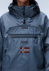 Light blue hooded jacket with a half-zip, front pouch pocket, and a Norwegian flag patch. Features textured fabric and adjustable drawstrings.