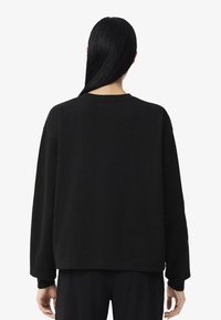 Sweatshirt preto oversized com mangas longas, decote redondo e punhos canelados. Tecido suave com silhueta casual, vista de trás mostrada.