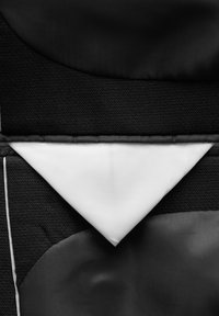 Texturiertes schwarzes Gewebe mit weißen dreieckigen Akzenten. Besteht aus glatten und gewebten Materialien, hat eine strukturierte Form und kontrastierende Muster.