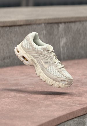 Light beige athletic shoe with a mesh upper, rounded toe, and textured midsole. Features padded collar and lacing with a subtle logo.