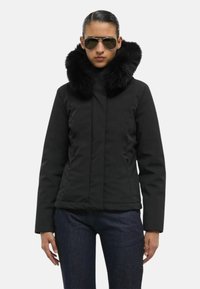 Giacca nera con un collo in morbida pelliccia sintetica; presenta una chiusura lampo frontale, due tasche laterali e maniche lunghe; abbinata a jeans scuri.