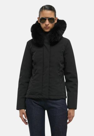 Giacca nera con un collo in morbida pelliccia sintetica; presenta una chiusura lampo frontale, due tasche laterali e maniche lunghe; abbinata a jeans scuri.