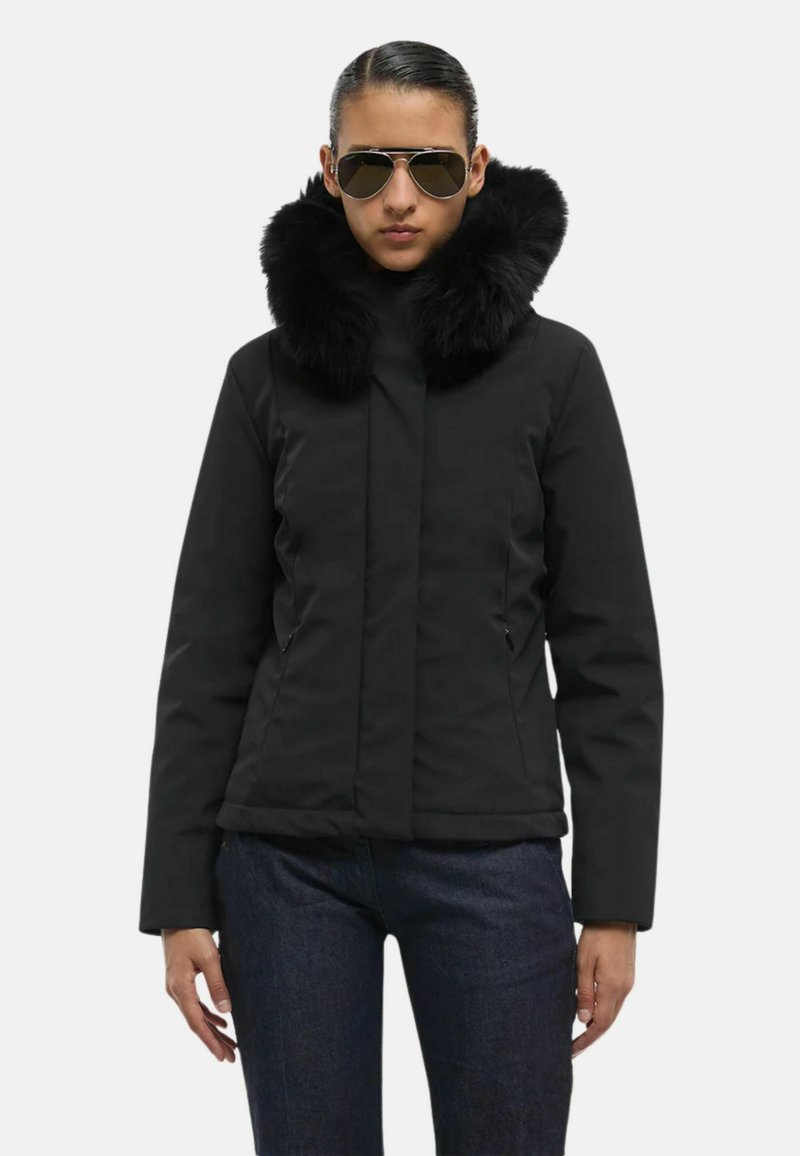 Giacca nera con un collo in morbida pelliccia sintetica; presenta una chiusura lampo frontale, due tasche laterali e maniche lunghe; abbinata a jeans scuri.